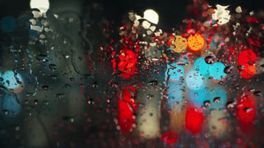 Akşam şehrinin çok renkli ışıkları ve yağmurlu bir pencereden geçen arabalar. Yağmurlu depresif hava