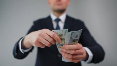 Resmi olarak giyinmiş bir adam Amerikan dolarlarını yavaşça kameraya doğru fırlatıyor. Yatırım, başarı, finansal beklentiler veya kariyer ilerlemesi kavramı.