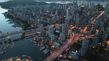 Geceleri Vancouver 'ın merkezindeki göz kamaştırıcı hava manzarası. Gökdelenler ve yollardaki trafik, Granville Köprüsü ve İngiliz Körfezi. Dağlar arka planda görünür. British Columbia, Kanada.