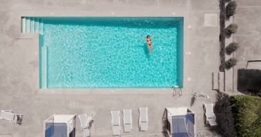 Havuz kenarındaki minimalist dekorlar ve boş şezlonglarla çevrili havuz başında dinlenen insan manzarası..