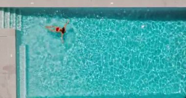 Top down view of a woman in red swimsuit swimming in the pool. Summer lifestyle