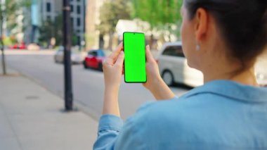Kadın sokakta dikiliyor ve yeşil ekranlı akıllı telefon kullanıyor. İletişim, iş günü, yoğun yaşam konsepti.