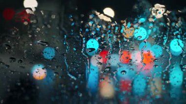 Akşam şehrinin çok renkli ışıkları ve yağmurlu bir pencereden geçen arabalar. Yağmurlu depresif hava