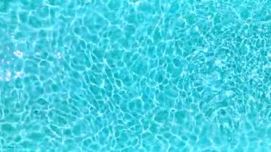 Yüzme havuzundaki saf mavi suyun yüzeyinde ışık yansımaları var. Hava görüntüleri, yukarıdan aşağıya doğru. Yavaş çekim