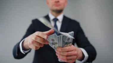 Resmi olarak giyinmiş bir adam Amerikan dolarlarını yavaşça kameraya doğru fırlatıyor. Yatırım, başarı, finansal beklentiler veya kariyer ilerlemesi kavramı.