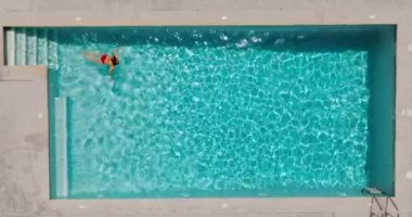 Top down view of a woman in red swimsuit swimming in the pool. Summer lifestyle