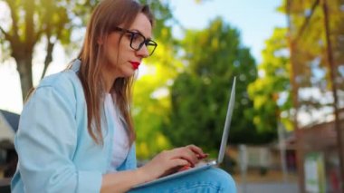 Kadın parkta oturuyor, dizüstü bilgisayarla çalışıyor ve kahve içiyor..