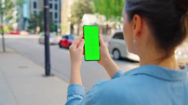 Kadın sokakta dikiliyor ve yeşil ekranlı akıllı telefon kullanıyor. İletişim, iş günü, yoğun yaşam konsepti.