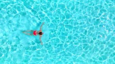 Top down view of a woman in red swimsuit swimming in the pool. Summer lifestyle.