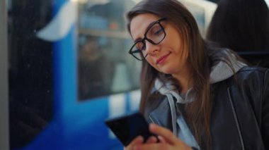 Toplu taşıma. Tramvayda akıllı telefon kullanan, arkadaşlarıyla mesajlaşan bir kadın. Şehir, şehir, ulaşım. Yavaş çekim