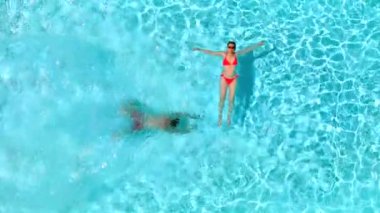 Çift havuzda rahatlar. Kadın sırtüstü yatarken bir erkeğin havuza dalıp yüzmesi. Yavaş çekim