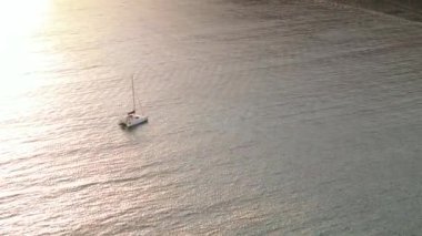 Yelkenlinin kayalık kıyıya yakın derin mavi bir denizde yelken açtığını gösteren hava görüntüleri. Drone 'dan deniz burnu. İtalya, Sardinya 'da gün batımı. Seyahat videosu
