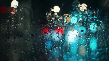 Akşam şehrinin çok renkli ışıkları ve yağmurlu bir pencereden geçen arabalar. Yağmurlu depresif hava