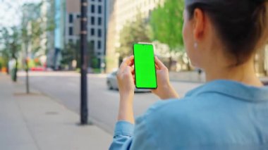 Kadın sokakta dikiliyor ve yeşil ekranlı akıllı telefon kullanıyor. İletişim, iş günü, yoğun yaşam konsepti. Yörünge atışı