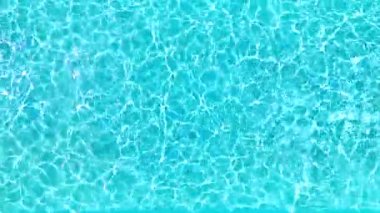 Yüzme havuzundaki saf mavi suyun yüzeyinde ışık yansımaları var. Hava görüntüleri, yukarıdan aşağı görünüm.