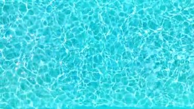 Yüzme havuzundaki saf mavi suyun yüzeyinde ışık yansımaları var. Hava görüntüleri, yukarıdan aşağıya doğru. Yavaş çekim