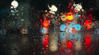 Akşam şehrinin çok renkli ışıkları ve yağmurlu bir pencereden geçen arabalar. Yağmurlu depresif hava