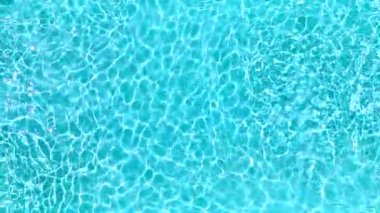 Yüzme havuzundaki saf mavi suyun yüzeyinde ışık yansımaları var. Hava görüntüleri, yukarıdan aşağıya doğru. Yavaş çekim