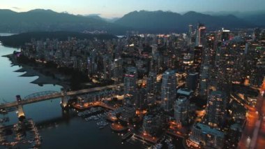 Geceleri Vancouver 'ın merkezindeki göz kamaştırıcı hava manzarası. Gökdelenler ve yollardaki trafik, Granville Köprüsü ve İngiliz Körfezi. Dağlar arka planda görünür. British Columbia, Kanada.
