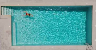 Top down view of a woman in red swimsuit swimming in the pool. Summer lifestyle.