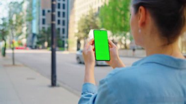Kadın sokakta dikiliyor ve yeşil ekranlı akıllı telefon kullanıyor. İletişim, iş günü, yoğun yaşam konsepti. Yörünge atışı