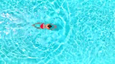 Top down view of a woman in red swimsuit swimming in the pool. Summer lifestyle.