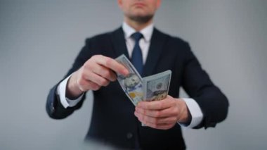 Resmi olarak giyinmiş bir adam Amerikan Doları 'nı kameraya doğru savuruyor. Yatırım, başarı, finansal beklentiler veya kariyer ilerlemesi kavramı.