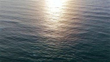 Gün batımında denizin ya da okyanusun mavi yüzeyinde uçmak. Güneş ışığı suya yansıyor. İHA atışı