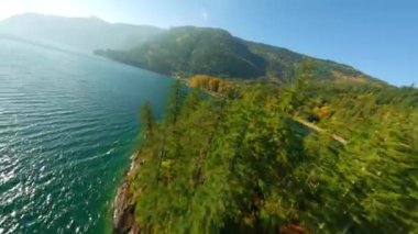 Harrison Gölü 'nün yüzeyinde hızlı bir uçuş. Göz kamaştırıcı sonbahar manzarası, dağ yamaçlarındaki renkli orman. British Columbia, Kanada. FPV insansız hava aracı tarafından filme alındı.
