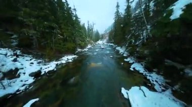 FPV insansız hava aracı kışın hızlı akan nehirde hızlı bir şekilde uçuyor. Etrafı çam ormanlarıyla çevrili. Whistler, British Columbia, Kanada yakınlarında çekilmiş..