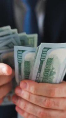 Resmi olarak giyinmiş bir adam Amerikan dolarlarını sayıyor, yakın plan. Yatırım, başarı, finansal beklentiler veya kariyer ilerlemesi kavramı.