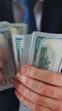 Resmi olarak giyinmiş bir adam Amerikan dolarlarını sayıyor, yakın plan. Yatırım, başarı, finansal beklentiler veya kariyer ilerlemesi kavramı.