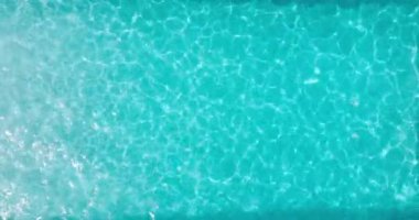 Yüzme havuzundaki saf mavi suyun yüzeyinde ışık yansımaları var. Hava görüntüleri, yukarıdan aşağıya doğru. Yavaş çekim