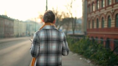 Beyaz ceketli bir iş kadını, sabahın erken saatlerinde şehirde dolaşıyor, kahve içiyor ve akıllı telefon kullanıyor. İletişim, iş günü, yoğun yaşam konsepti. Arka plan.