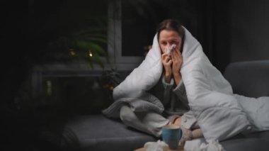 Hasta kız grip olmuş ya da nezle olmuş, alerji belirtileri gösteriyor. Alerjisi olan genç bir kadın mendil içinde hapşırıyor, burnunu siliyor ve çay içiyor. Sağlıksız kadın mevsimsel virüs hastalığından muzdarip..