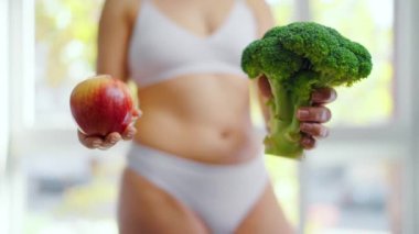 Elinde brokoli ve elma tutan bir kadın var. Hangisinin daha iyi olduğuna o karar verir. Sağlıklı beslenme kavramı.