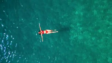 Kırmızı mayo giymiş bir kadının havadan görünüşü, kristal berrak deniz sularında rahatlama somutlaştırıcı bir şekilde zahmetsizce sırt üstü yüzüyor. Yaz tatilleri.