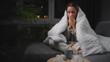 Hasta kız grip olmuş ya da nezle olmuş, alerji belirtileri gösteriyor. Alerjisi olan genç bir kadın mendil içinde hapşırıyor, burnunu siliyor ve çay içiyor. Sağlıksız kadın mevsimsel virüs hastalığından muzdarip..