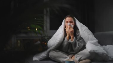 Hasta kız grip olmuş ya da nezle olmuş, alerji belirtileri gösteriyor. Alerjisi olan genç bir kadın mendil içinde hapşırıyor, burnunu siliyor ve çay içiyor. Sağlıksız kadın mevsimsel virüs hastalığından muzdarip..