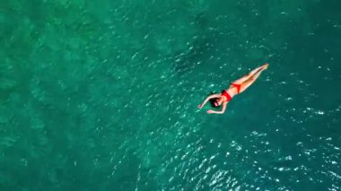 Kırmızı mayo giymiş bir kadının hava görüntüsü, kristal berrak deniz sularında rahatlama somutlaştırıcı bir şekilde sırtüstü uzanır. Yaz tatilleri.