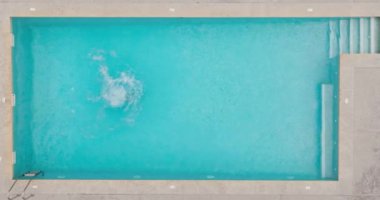 Top down view as a man dives into the pool and swims. Slow motion