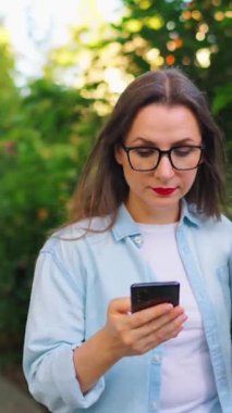 Dizüstü bilgisayarı ve akıllı telefonu olan mutlu bir kadın çiçek açan bahçede ya da işten sonra yeşil sokakta yürüyor..