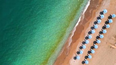 Mavi güneş şemsiyeleri ve turkuaz deniz suyuyla cennet gibi kumlu sahil manzarası..