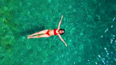 Kırmızı mayo giymiş bir kadının hava görüntüsü, kristal berrak deniz sularında rahatlama somutlaştırıcı bir şekilde sırtüstü uzanır. Yaz tatilleri.
