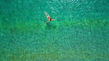 Kırmızı mayo giymiş bir kadının hava görüntüsü kristal berrak deniz sularında yüzüyor, rahatlama somutlaştırıyor. Yaz tatilleri.