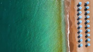 Mavi güneş şemsiyeleri ve turkuaz deniz suyuyla cennet gibi kumlu sahil manzarası..