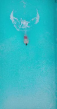 Bir adamın havuza dalıp, yavaş çekimde yüzdüğü tepeden aşağı bir manzara.