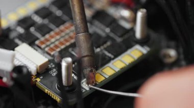 İHA kontrol panelinde lehimleme için hazırlanan bir kabloyu aşırı yakın çekim makro görüntüsü. Fpv insansız hava aracının mikroçipindeki lehimleme bağlantıları süreci.