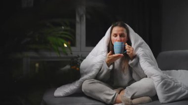 Hasta kız grip olmuş ya da nezle olmuş, alerji belirtileri gösteriyor. Alerjisi olan genç bir kadın mendil içinde hapşırıyor, burnunu siliyor ve çay içiyor. Sağlıksız kadın mevsimsel virüs hastalığından muzdarip..