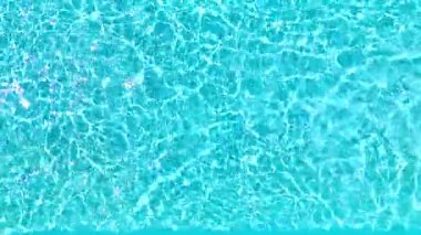 Yüzme havuzundaki saf mavi suyun yüzeyinde ışık yansımaları var. Hava görüntüleri, yukarıdan aşağı görünüm. 